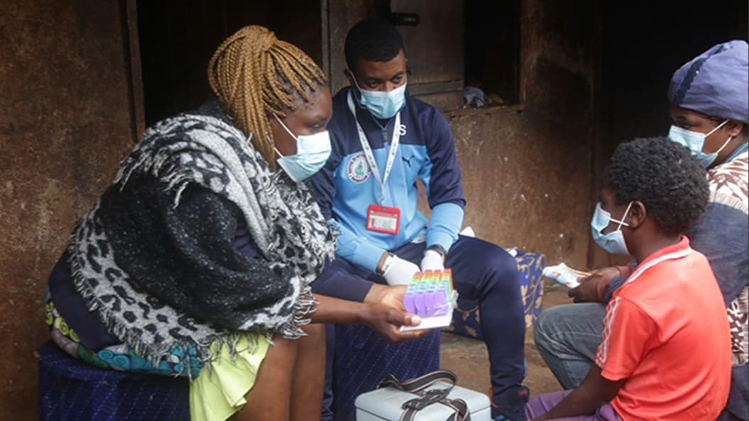 A woman holding a monthly pill organizer sits next to a representative of Cameroon's Ministry of Health and across from a woman and child.