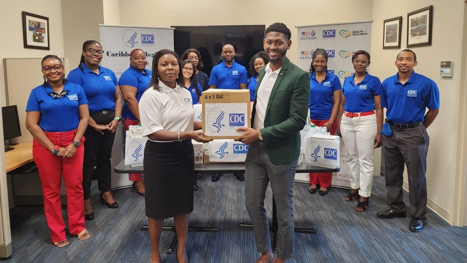 Group of 10 people, two stand at the front holding a box with the CDC/HHS logo