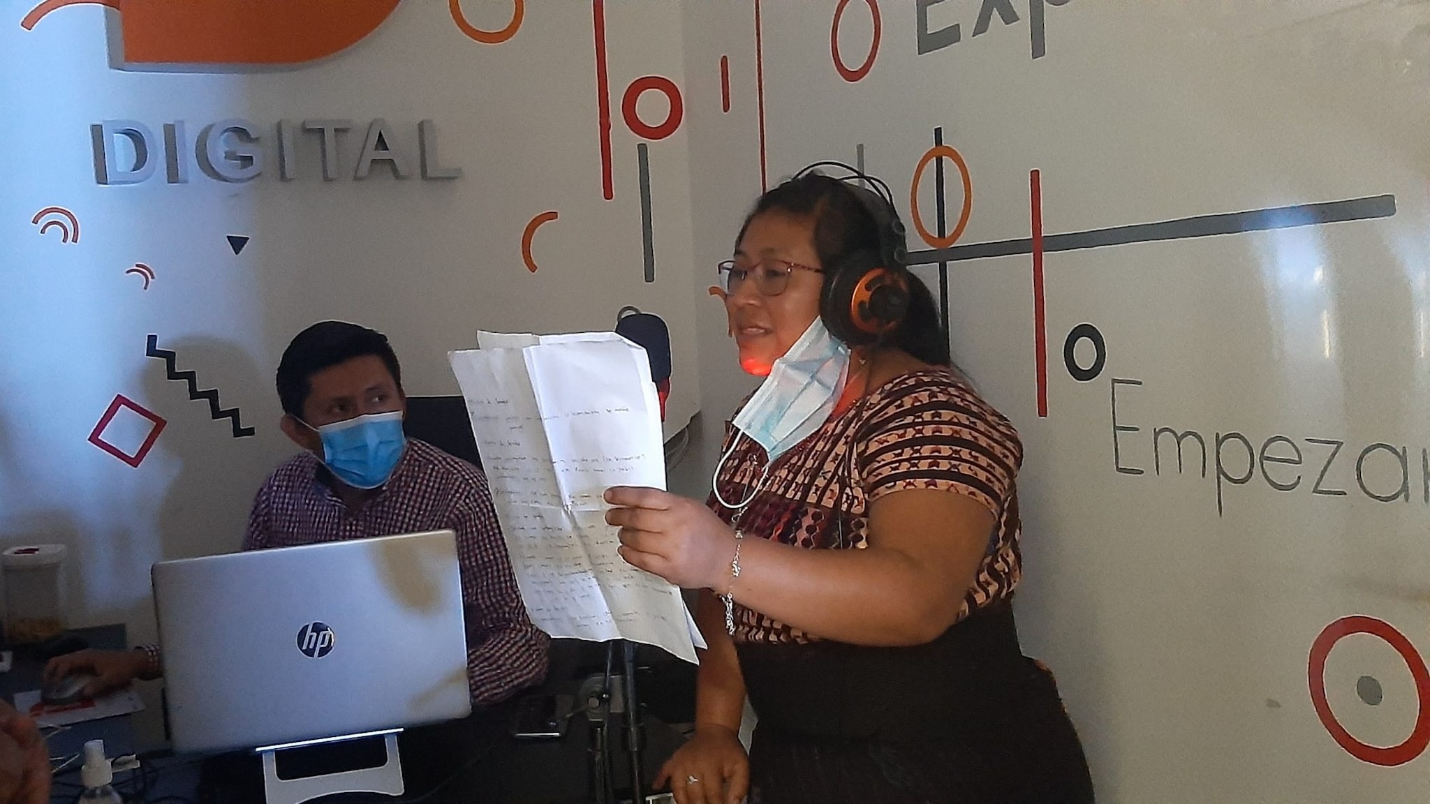 A woman is seen reading from a paper and speaking into a microphone to record a segment that will air on a local radio station.