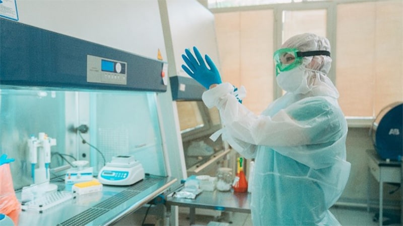Photo of a laboratorian wearing personal protective equipment while standing in front of a laboratory hood.
