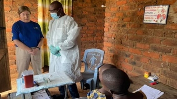 CDC Alison Johnson wearing a blue shit and beige pants and a man in a lab coat monitor field staff conducting an interview in a household in Tanzania.
