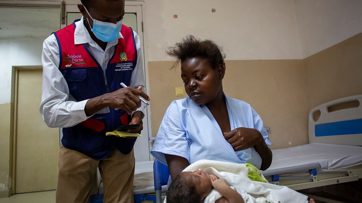 A mother holds her baby while a health care worker speaks to her.