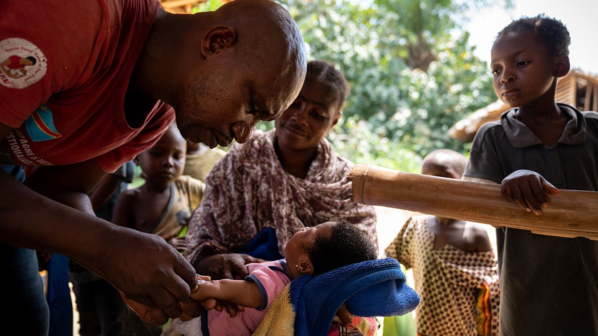 A health worker vaccinates an infant while the family watches