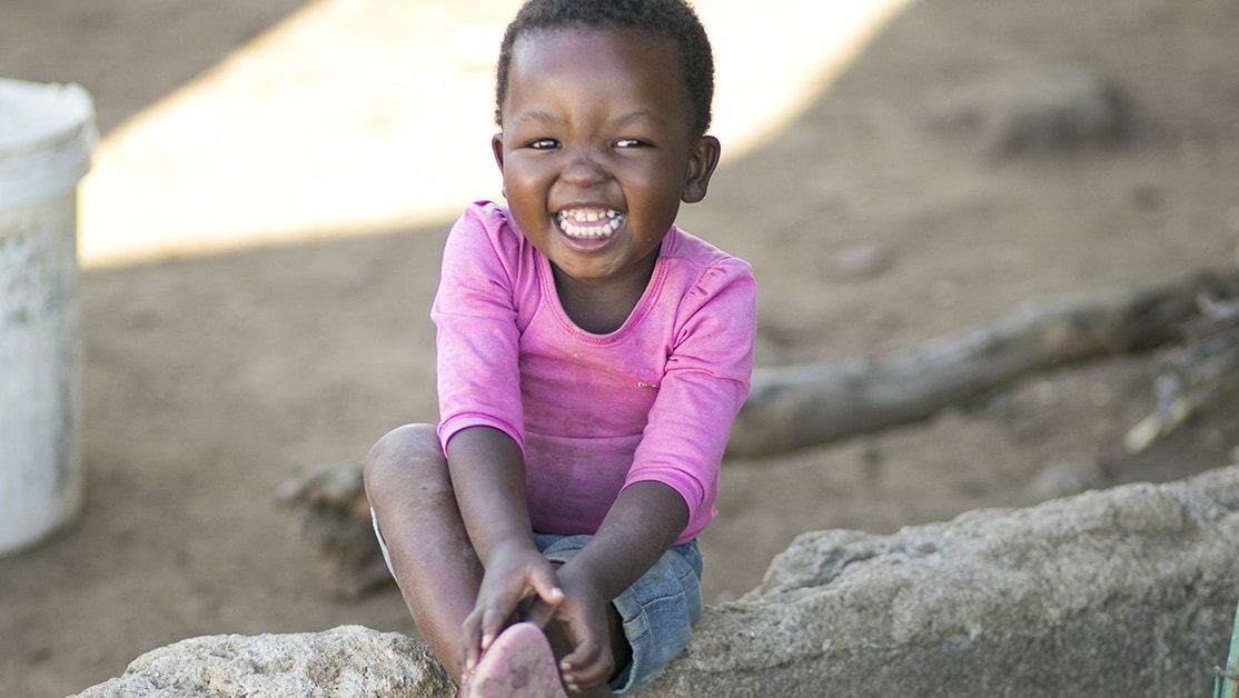 A girl in a pink shirt smiles while sitting.