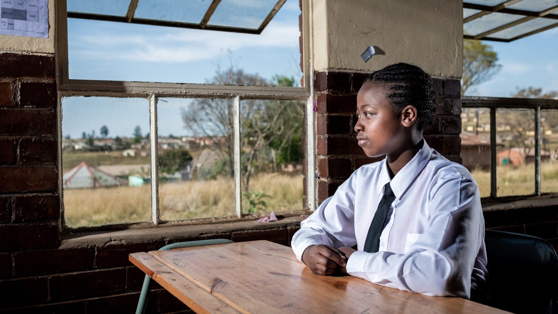 A girl in a white shirt sits at a desk looking out a window.