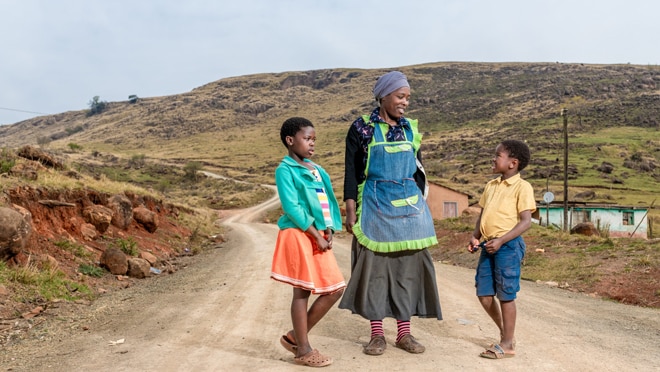 A woman walks on a dirt road with two children.