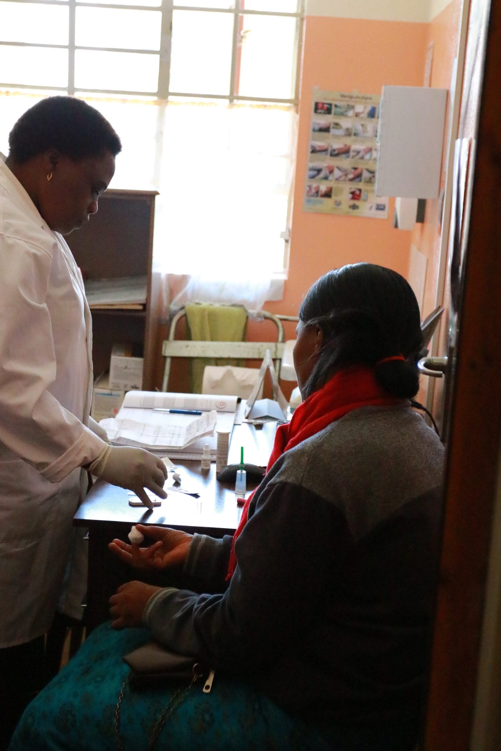 Healthcare professional stands and patient sits as she gets treated for HIV.