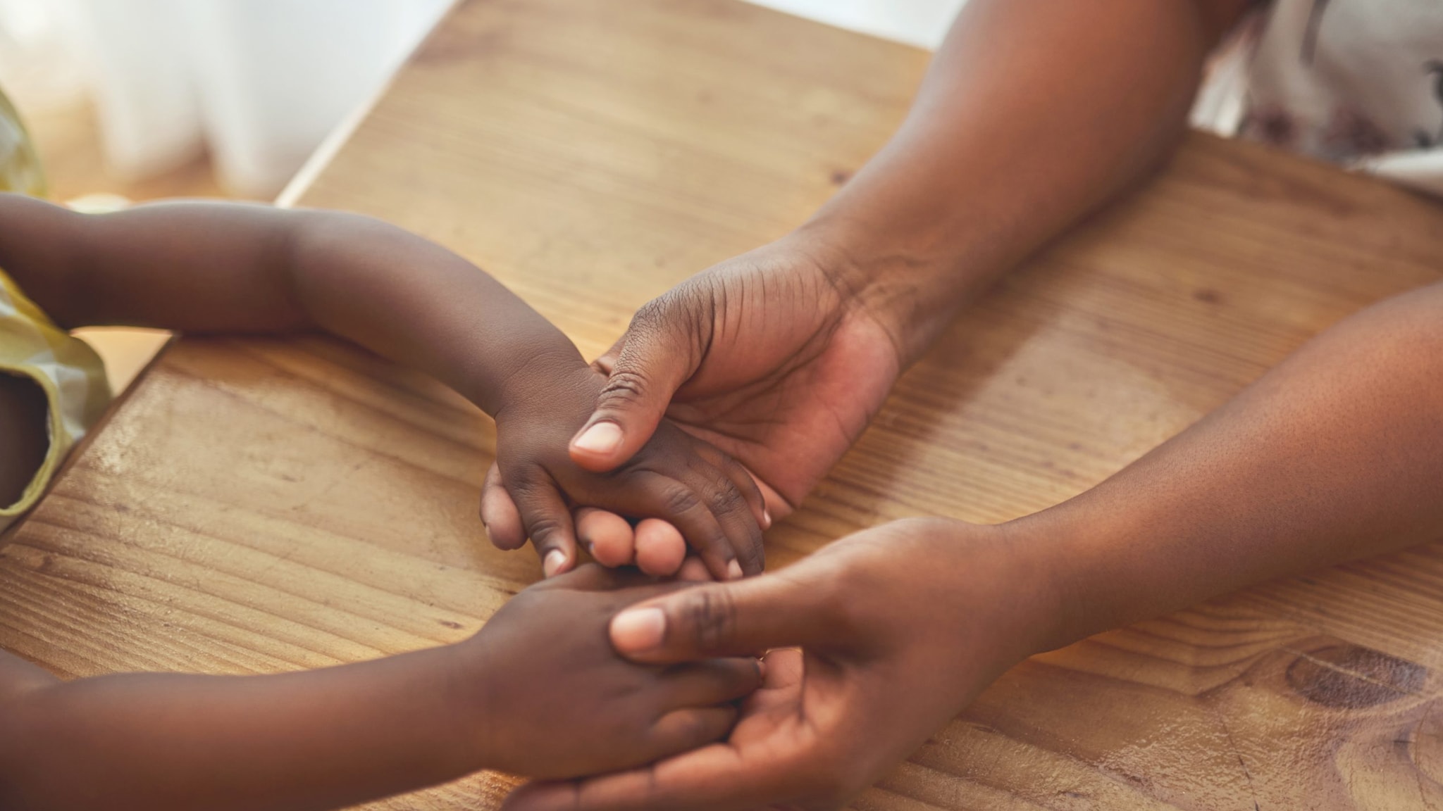 An adult holds the hands of a child at a table.