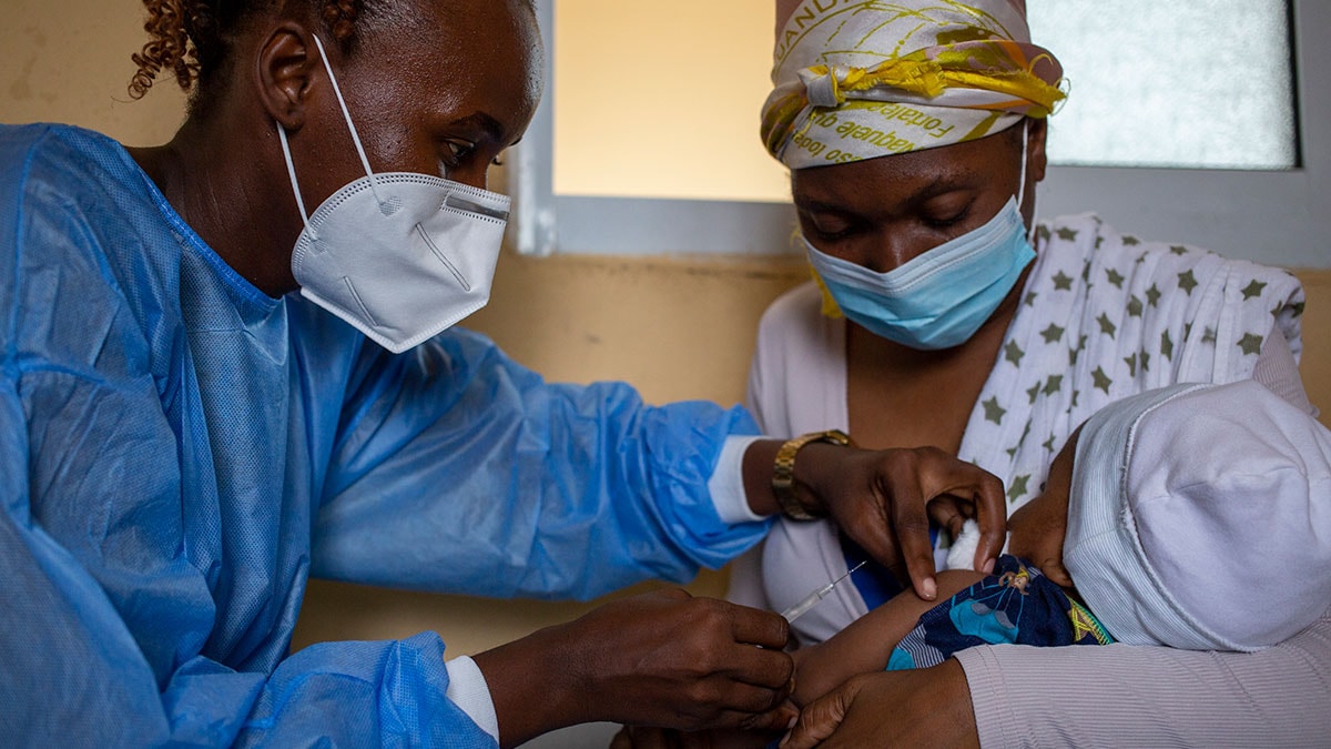 A mother in Angola holds her infant daughter while the child receives a dose of measles vaccine from a health care worker.