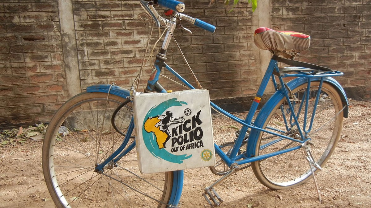 A bicycle stands in an African street with a Kick Polio Out of Africa bag over its handlebars.