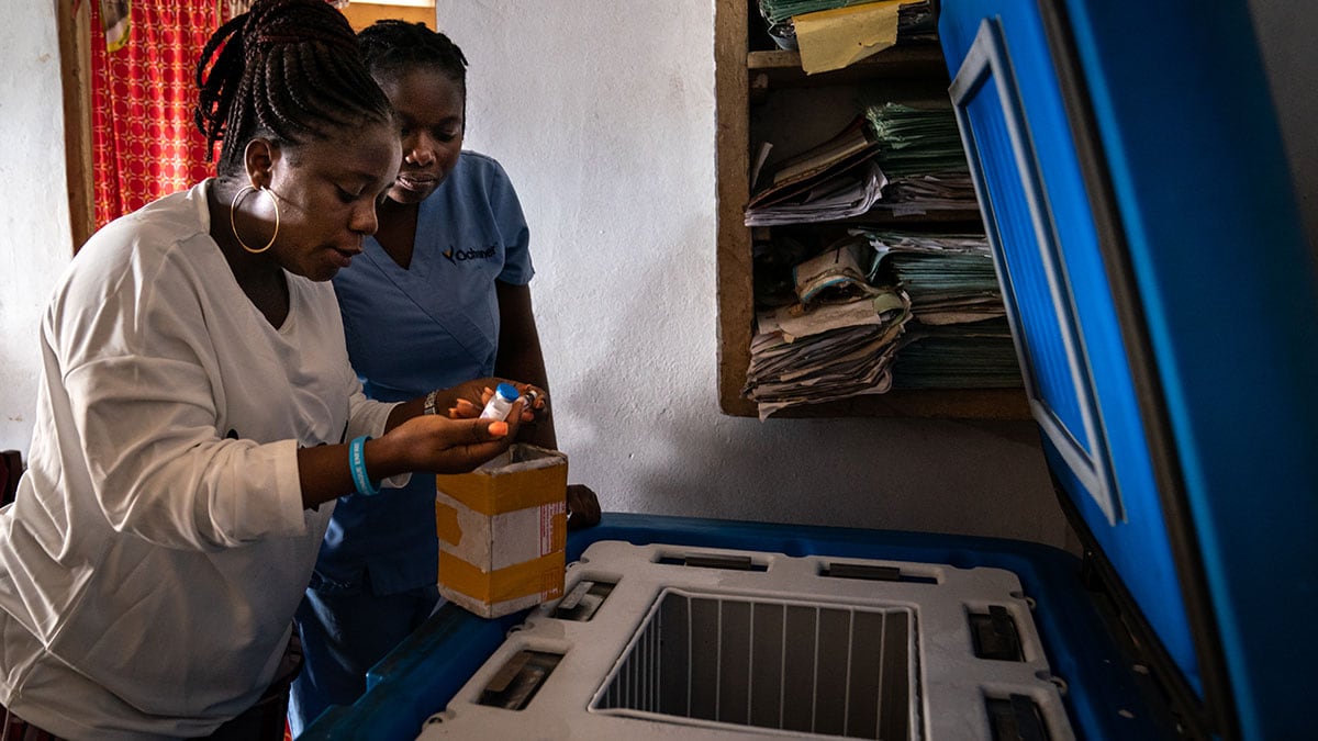 Two health care workers check vaccines in a storage refigerator.
