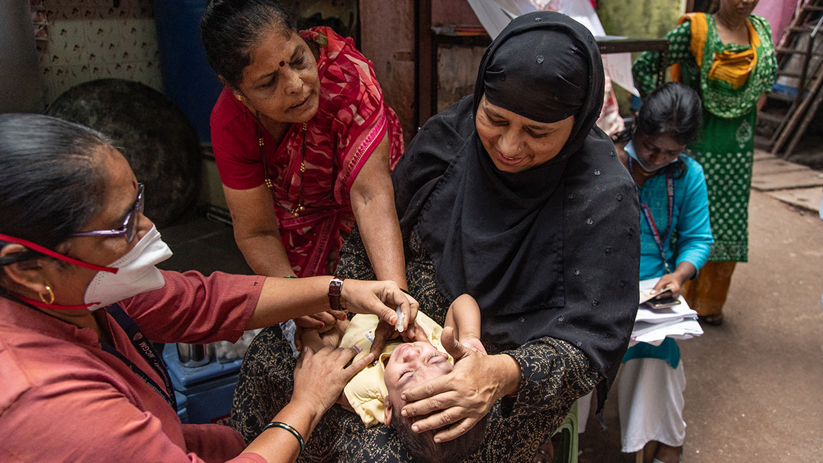 A 9-month-old receiving oral vaccinations from a female health care worker.