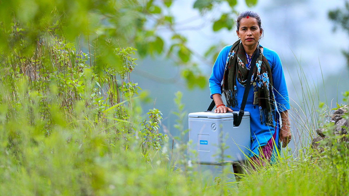 A woman carrying a cooler of vaccines walks in a remote area of Nepal.