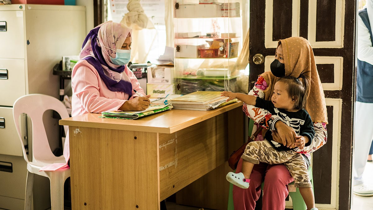Mother and daughter talk to health care worker in health center in the Philipines.