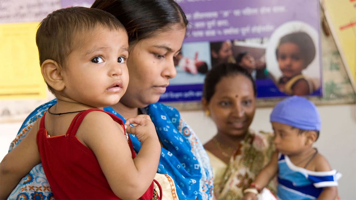 Two mothers hold their babies as they wait for vaccination in India.