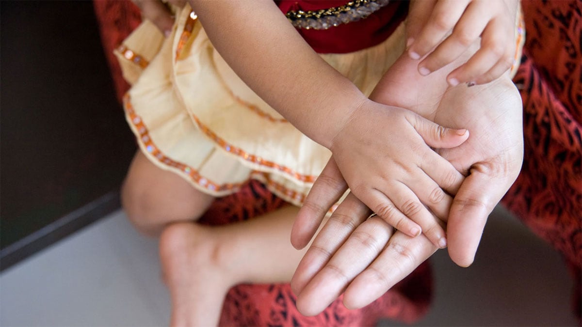 A young girl's hand rests in the hand of her mother as they wait for vaccination in India.