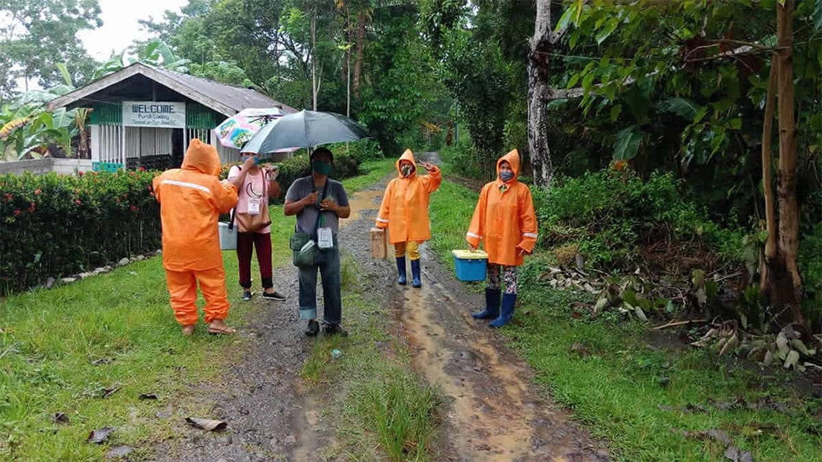 Four health workers carry vaccines through the rain in the Philippines.