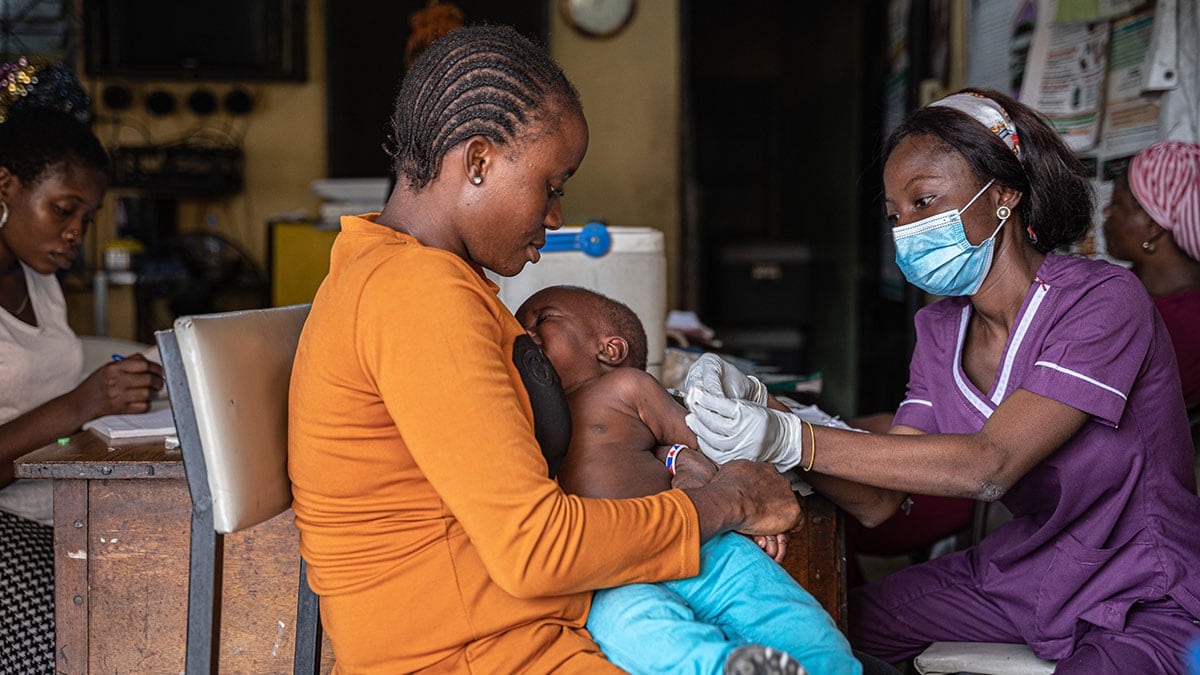 A mother holds her young son as a health work administers a vaccine to the child.