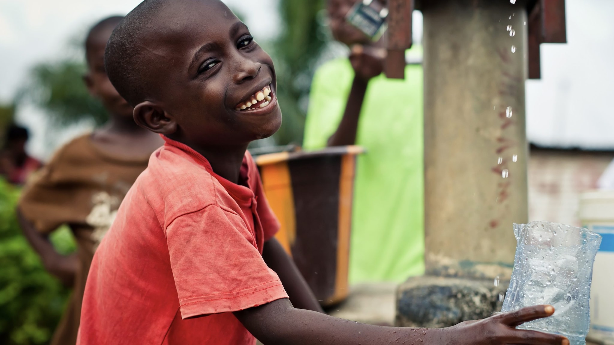 Boy holding glass getting drinking water from a pump