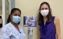 Nurse Dania Romero and CDC behavioral scientist Christina Craig wear surgical masks while standing next to a dispenser with alcohol-based hand rub.