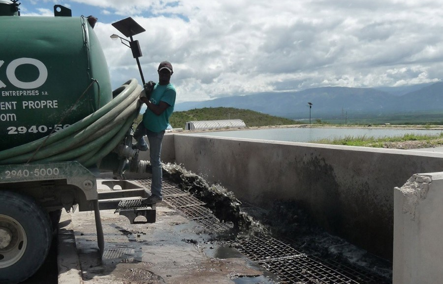 A man hangs from the front of a truck as sludge empties into a wastewater stabilization pond