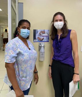 CDC Behavioral Scientist Christina Craig (right) and nurse Dania Romero (left) pose with a message-tested hand hygiene poster and new ABHR dispenser in regional hospital in Moca, Dominican Republic.