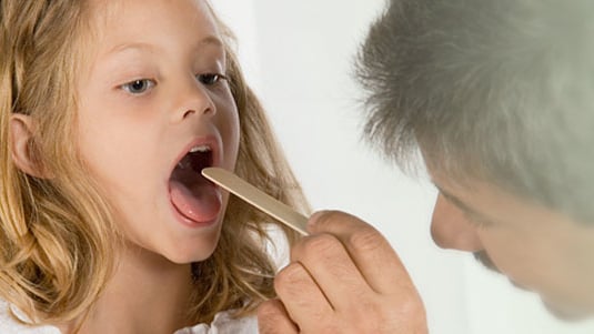 Un proveedor de atención médica examinando la garganta de una niña.