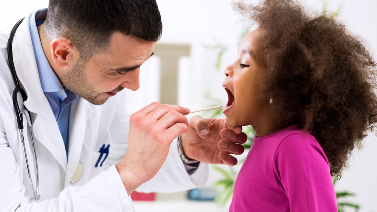 Un médico examinándole la garganta a una niña con un depresor de lengua.