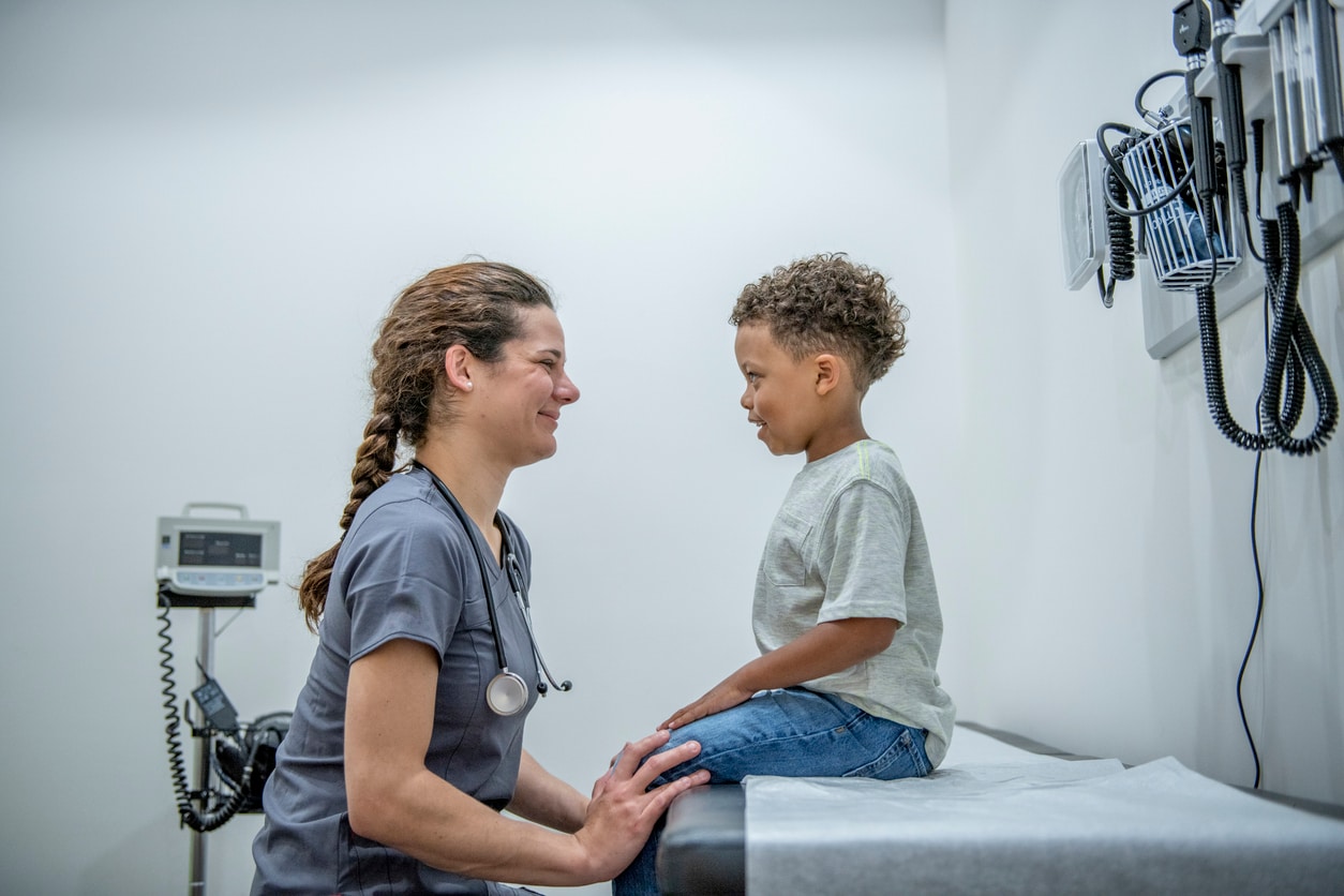 A young boy sitting on the examination table talking to a female doctor.