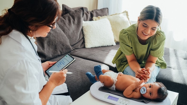 Baby on scale with health care provider and mother nearby .