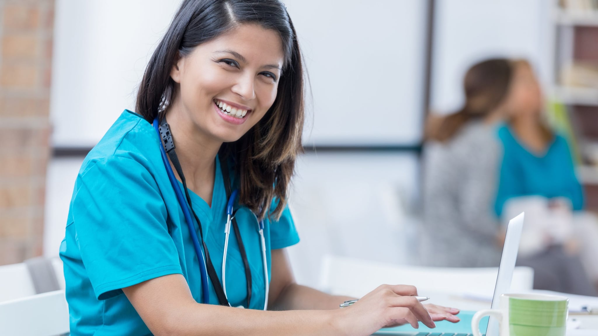 Medical professional sitting at desk and using a laptop computer.