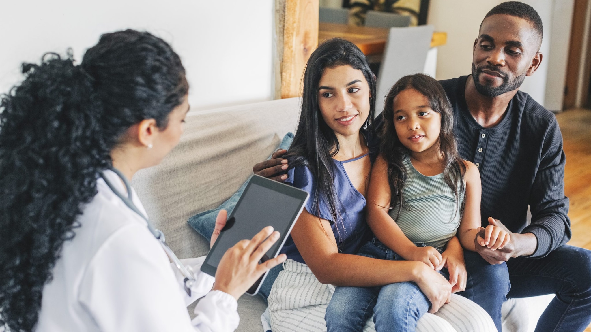 Health care provider holding a tablet and talking with a family of parents and their child.