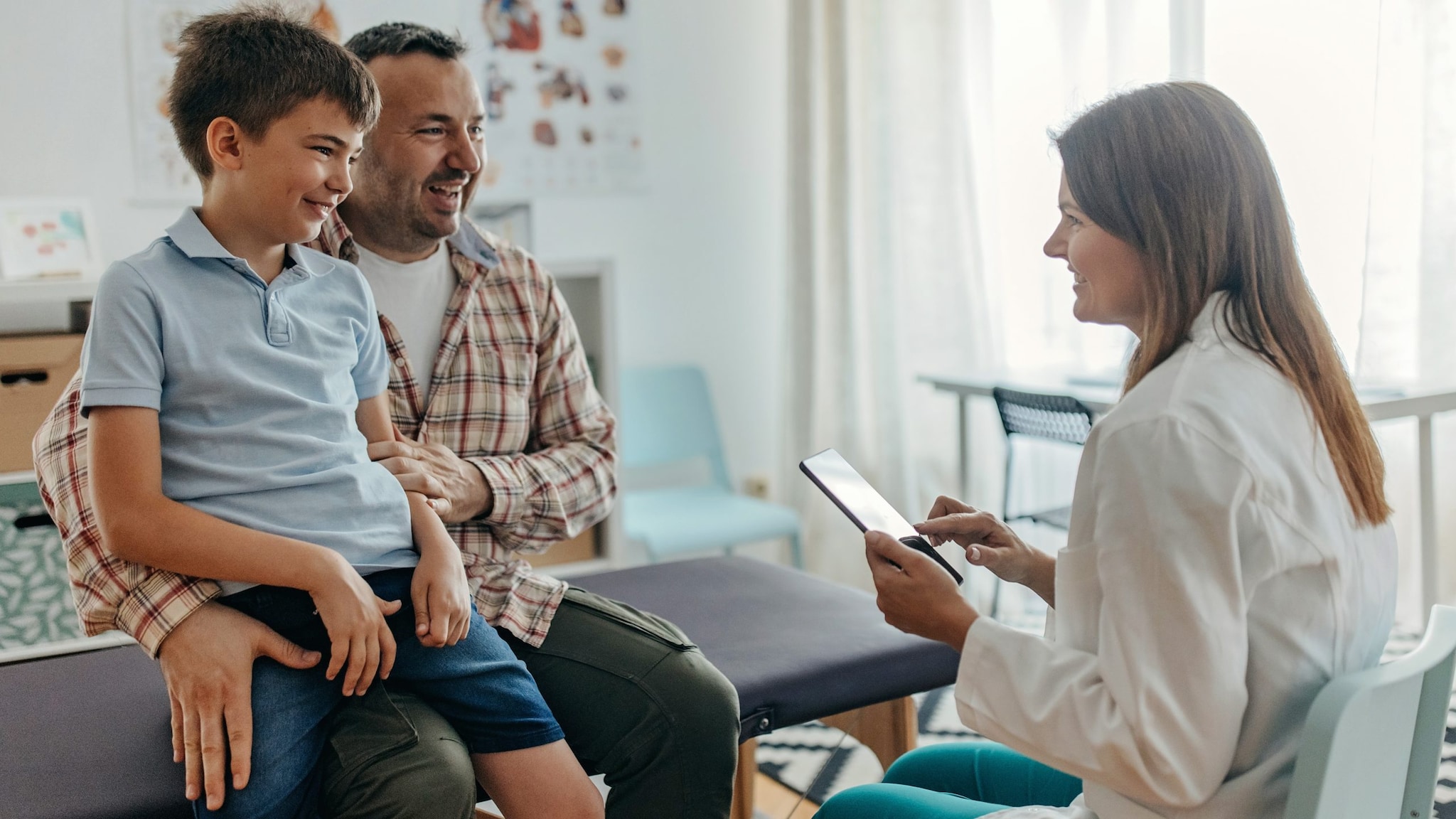 Health care provider goes over chart with father and son in a medical setting.