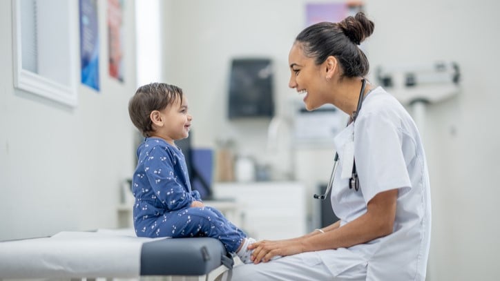 Toddler sitting on exam table and laughing with health care provider.