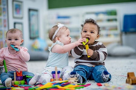 Three babies playing with blocks and putting toys in their mouths.