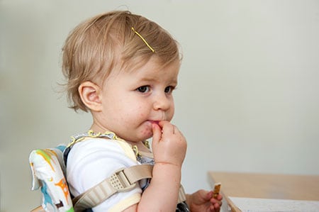 Toddler girl with red spots around the mouth, eating at a table.