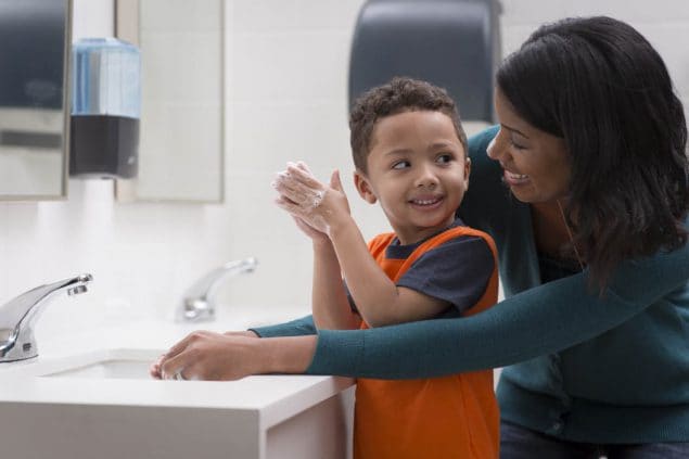 mom helping toddler boy wash his hands in a public restroom