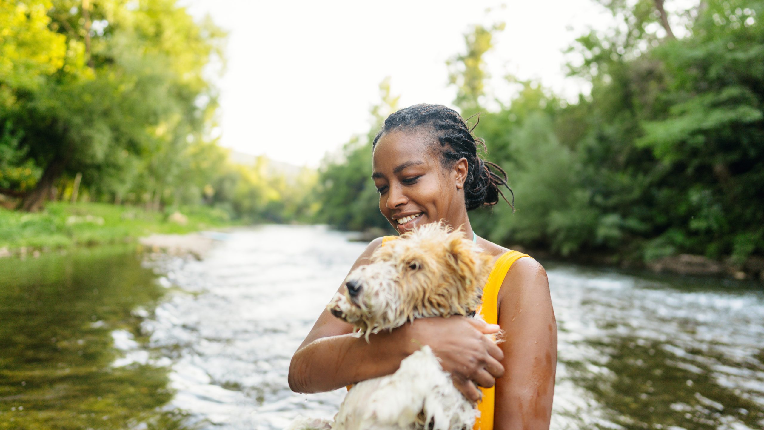 Smiling woman holding a dog with a river in the background