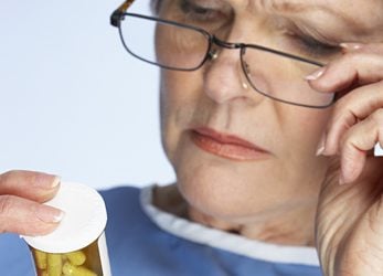 Woman reading sticker on pill bottle.