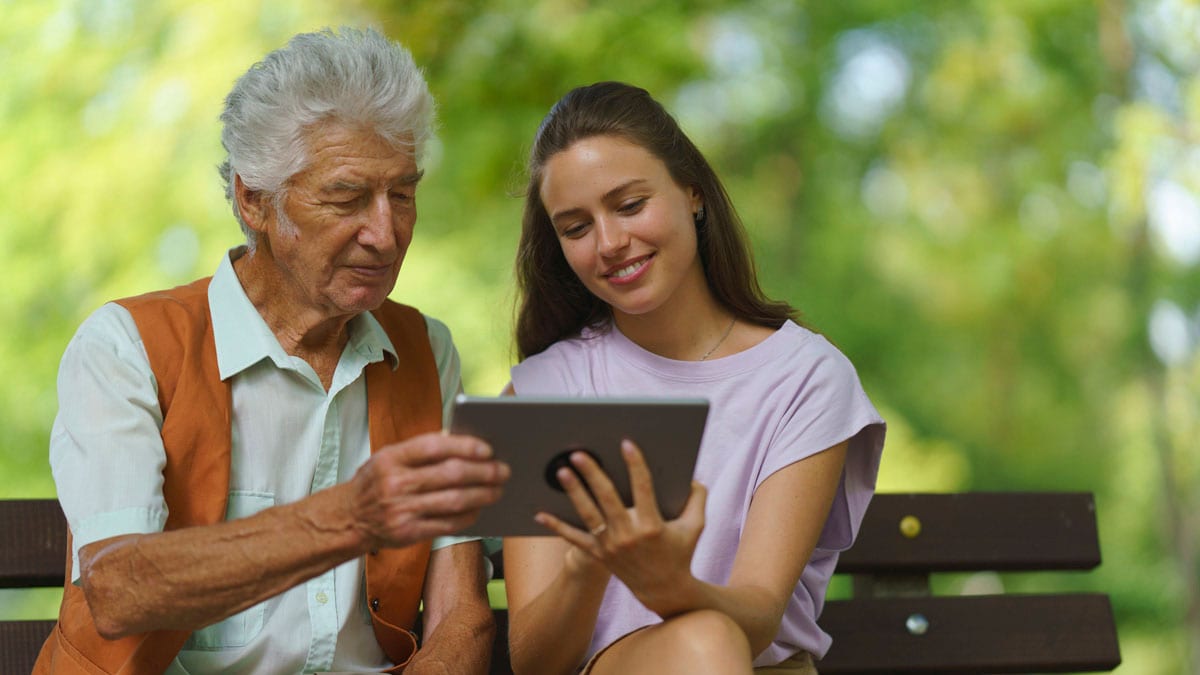 Caregiver helping senior man to shop online on tablet