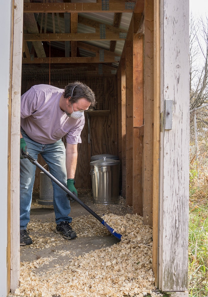 A person cleaning a barn while wearing protective equipment.