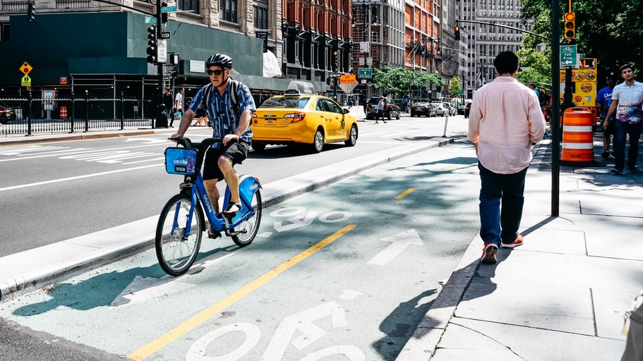 Cyclist in a bike lane in a large downtown area. A person is also walking nearby on a sidewalk.