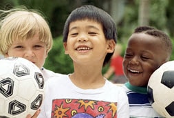 Three boys holding soccer balls, smiling.