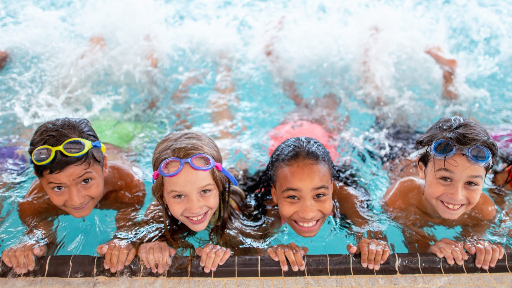 Children holding on to side of the pool while kicking their legs behind them.