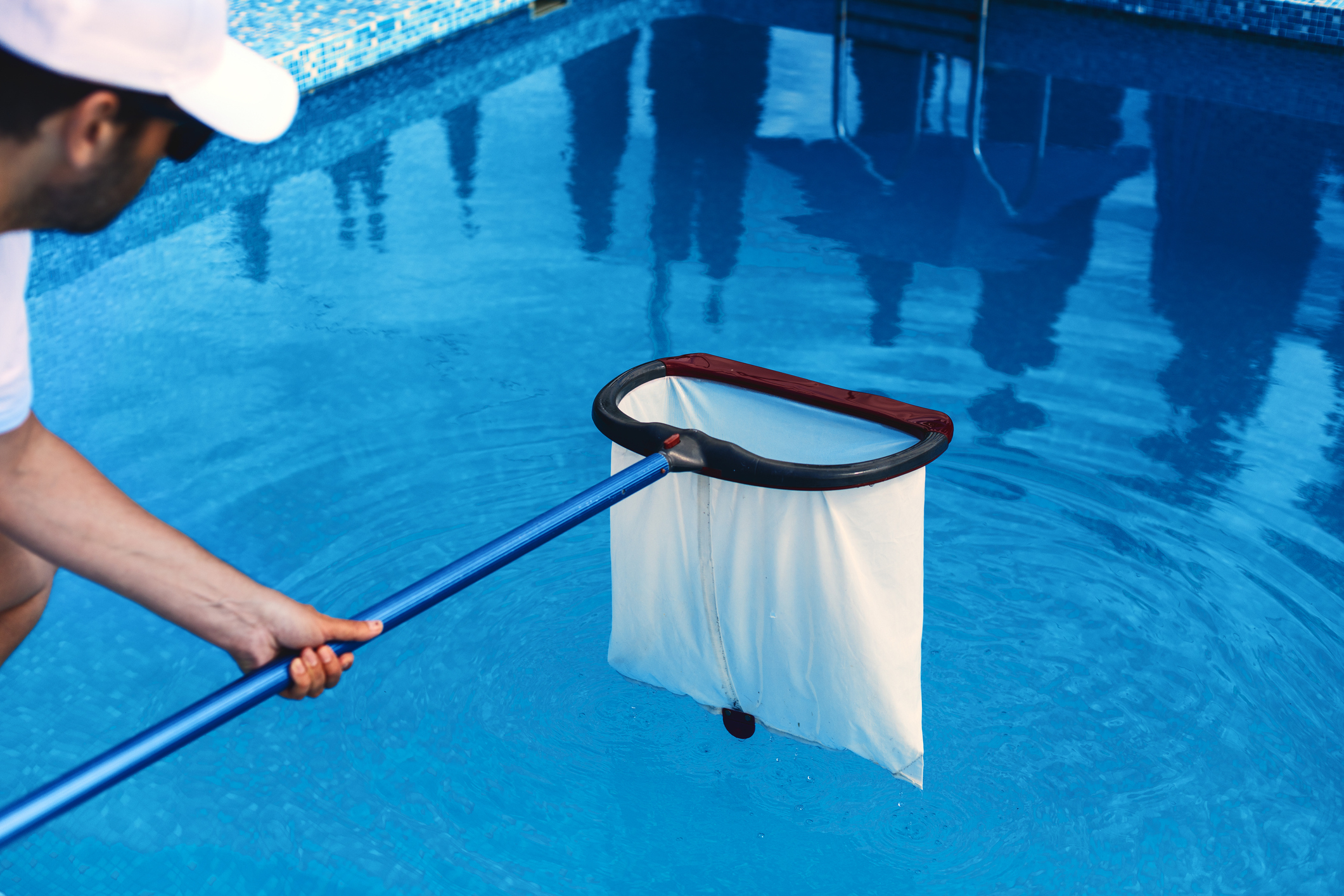 Hombre con una gorra sosteniendo una red de limpieza para piscinas sobre una piscina.