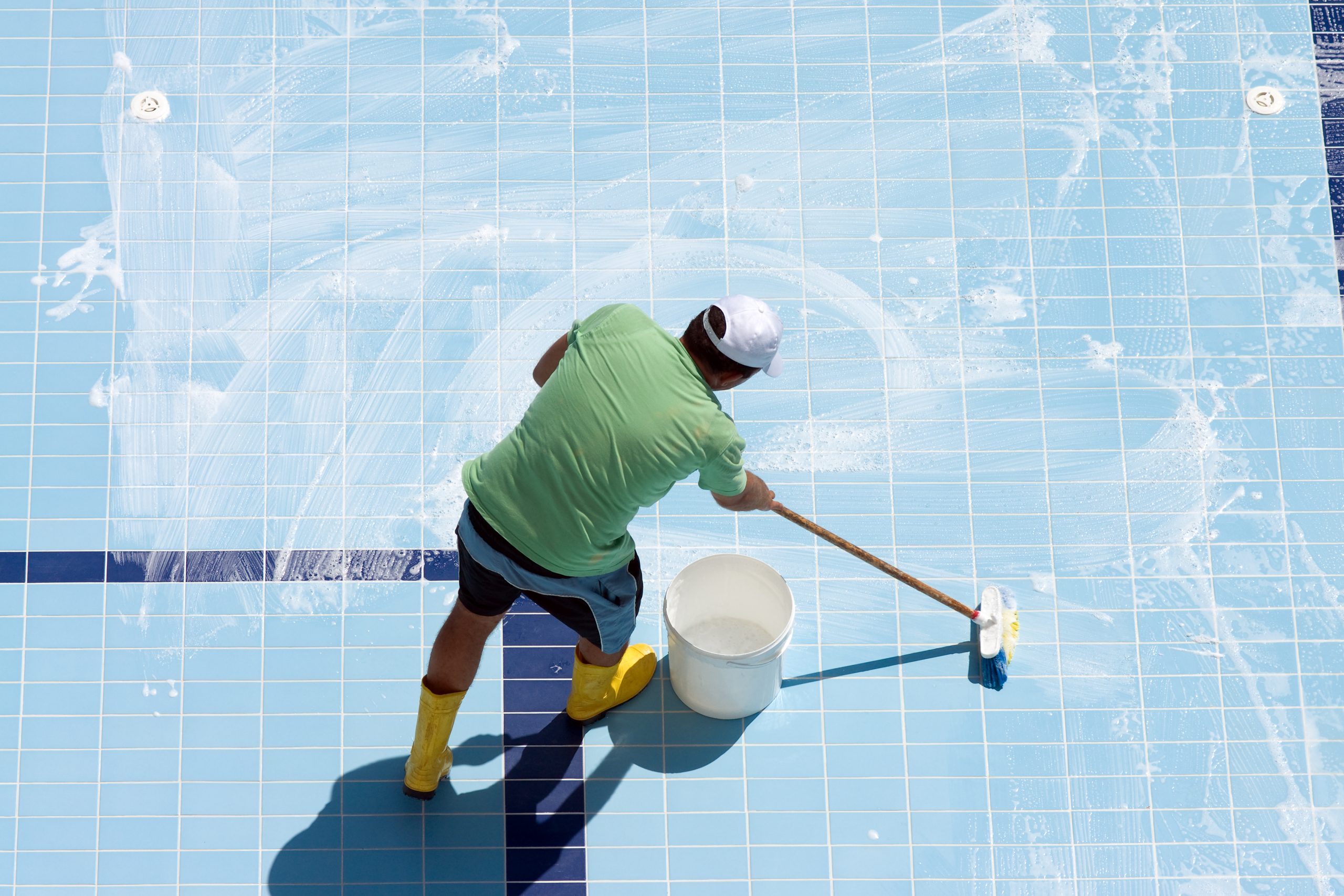 Hombre limpiando el fondo de una piscina vacía con un balde y un trapeador.