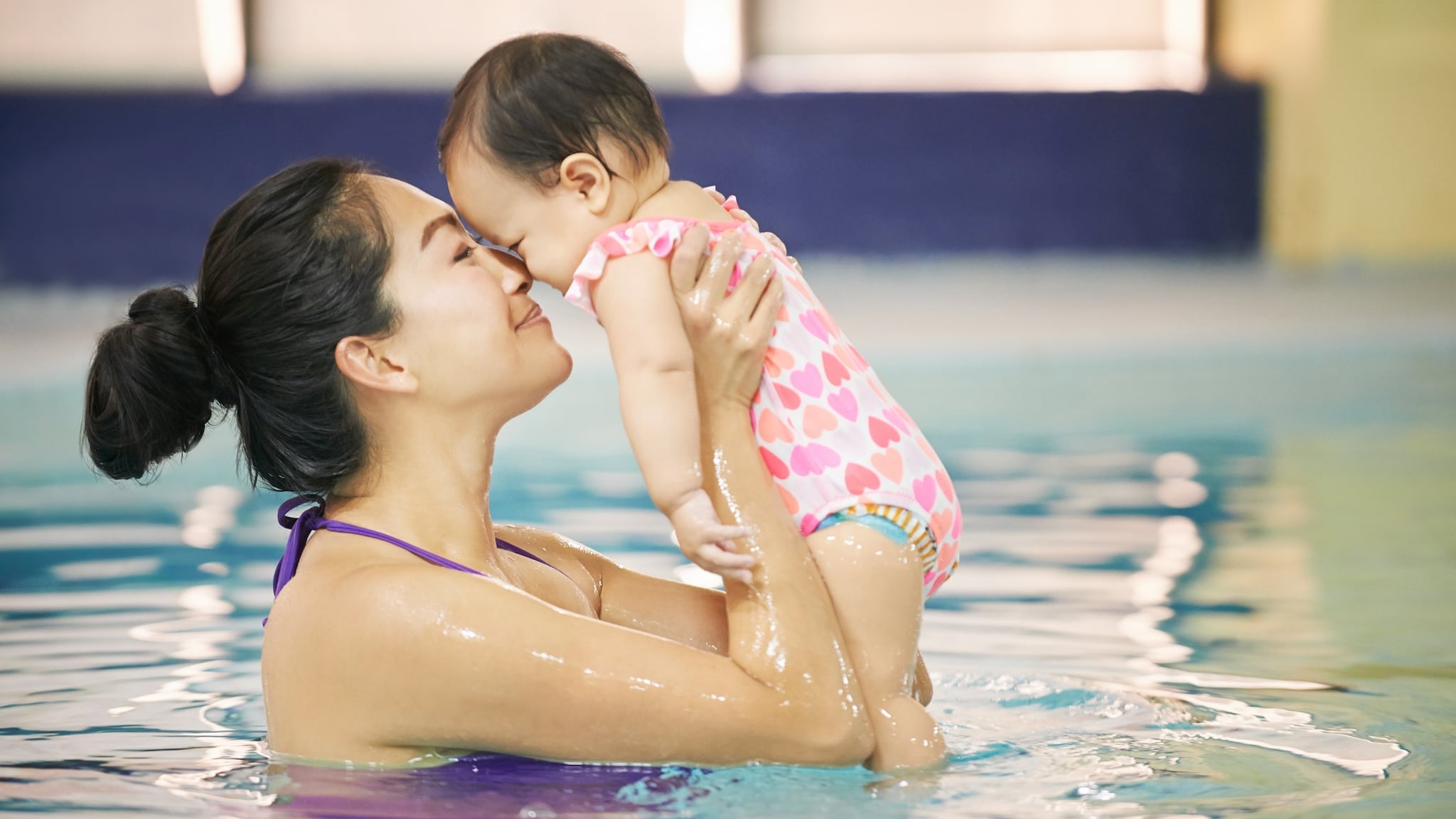 Mother in swimming pool holding baby that is wearing a swim diaper.