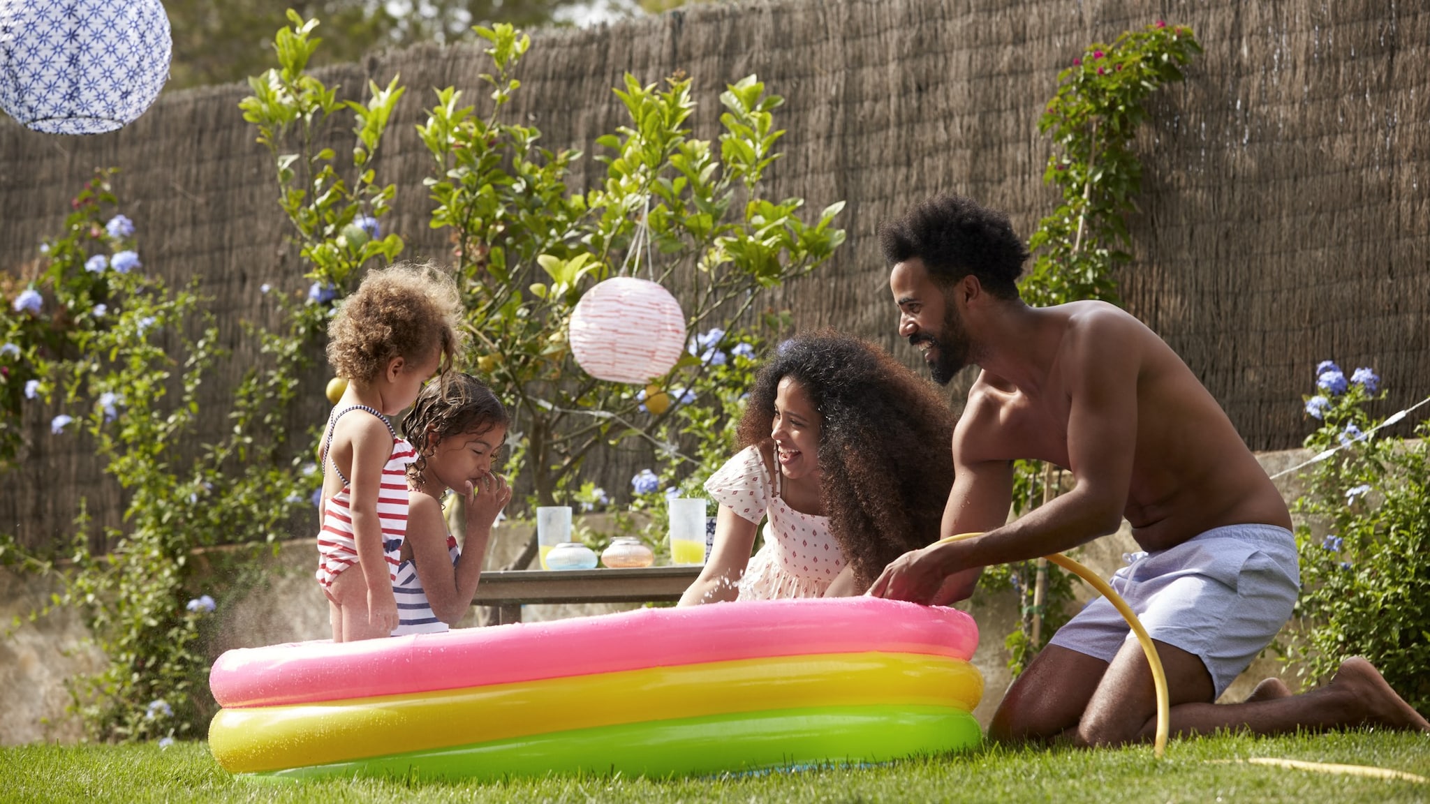 Una piscina para niños en un patio con dos niños pequeños adentro y sus padres afuera.