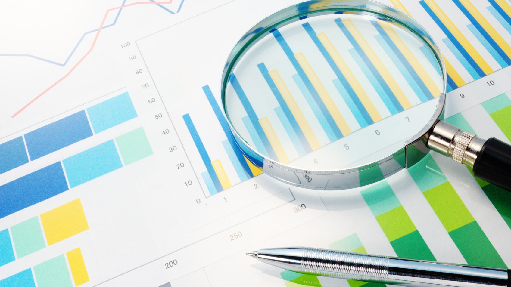 Silver pen and magnifying glass on top of blue and green charts and figures.