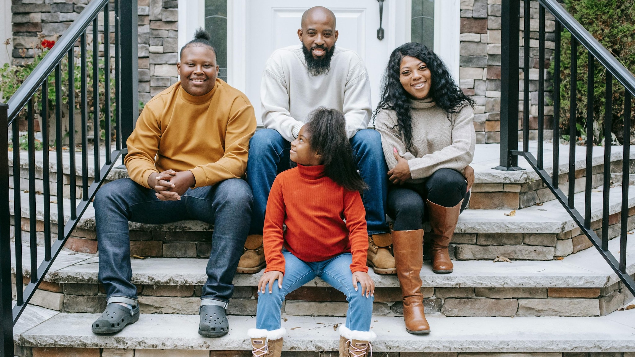 Two adults, one teen, and one youth, smiling and sitting on the steps in front of a house.